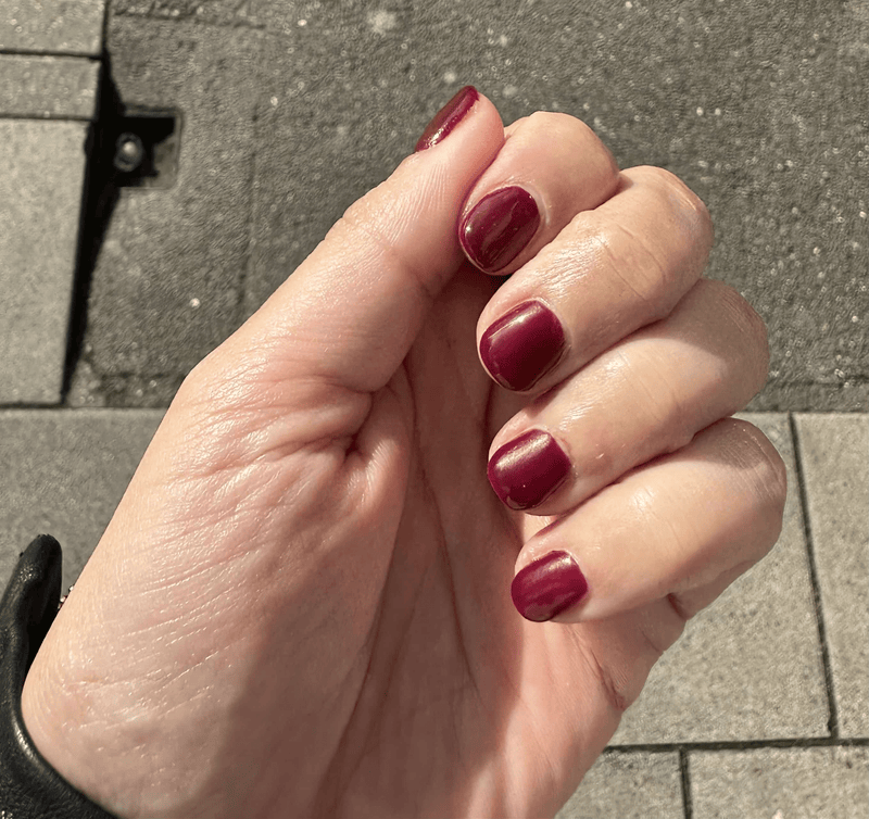 Hand displaying burgundy nail wraps in natural light showing deep red at-home manicure