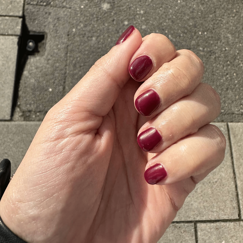 Hand displaying burgundy nail wraps in natural light showing deep red at-home manicure