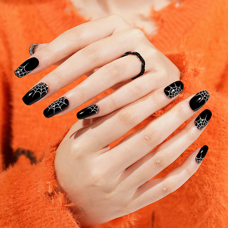 Glossy black press-on nails with white spiderweb accents, Halloween nail design.