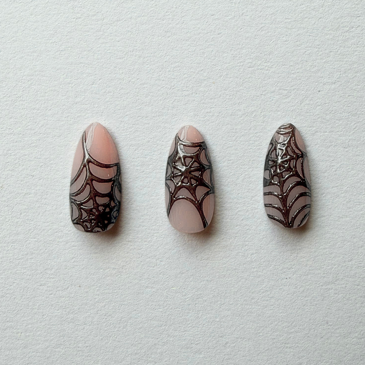 Nude press-on nails with black glittery spiderweb design, almond shape