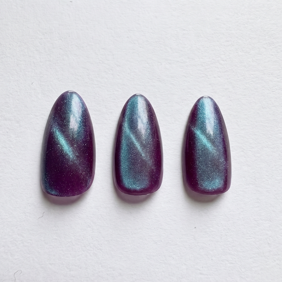 Short almond soft gel press-ons in deep purple with teal cat's-eye magnetic shimmer.