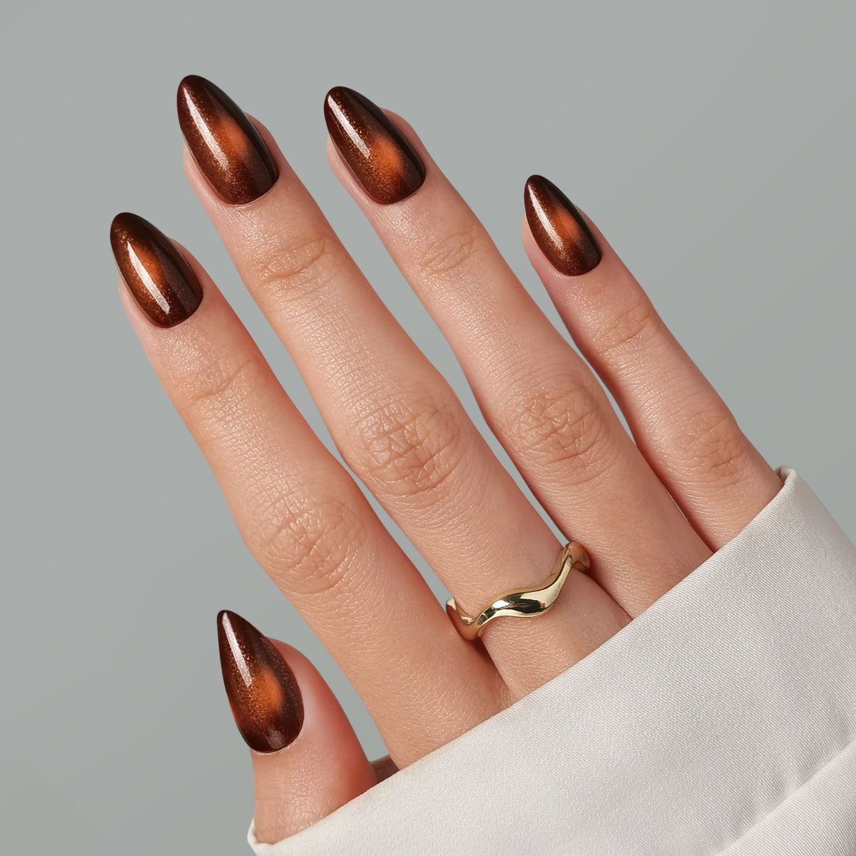 Almond press-on nails in deep brown with copper cat-eye shimmer, glossy finish.