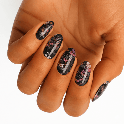 Dark floral nail wraps on hand featuring black base with pink botanical tree pattern