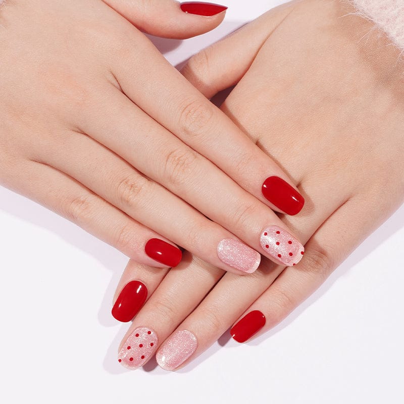 Red and pink polka dot gel nail wraps on hands showing romantic nail art design