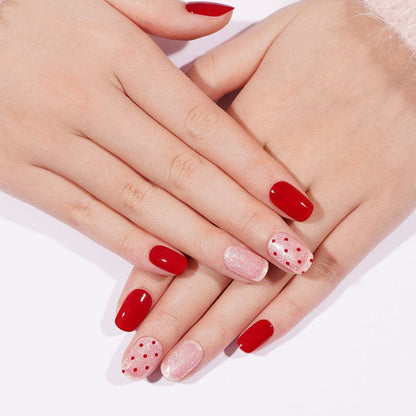 Red and pink polka dot gel nail wraps on hands showing romantic nail art design